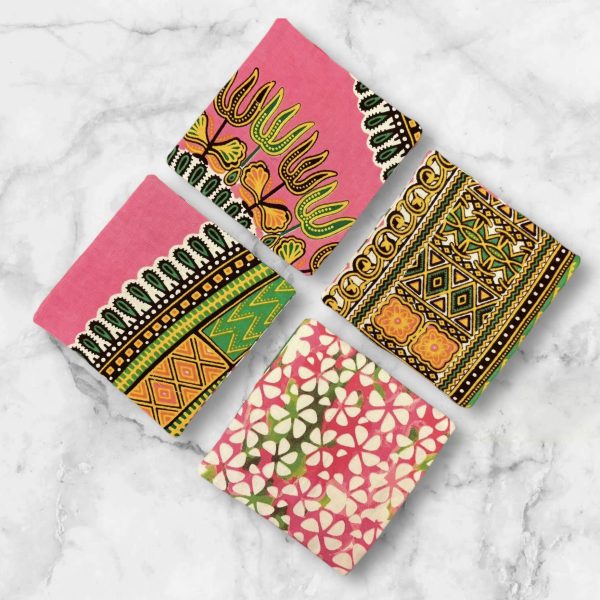 A set of four 4.5-inch square reversible fabric coasters with a pink and green African print on one side and a batik petal print on the other, displayed on a marble background.