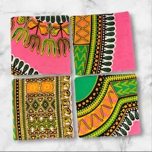 A set of four 4.5-inch square reversible fabric coasters with a pink and green African print on one side and a batik petal print on the other, displayed on a marble background.