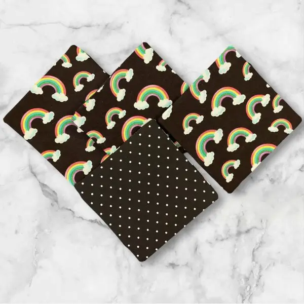 A set of four 4.5-inch square reversible fabric coasters with rainbow designs on one side and polka dots on the other, displayed on a marble background.