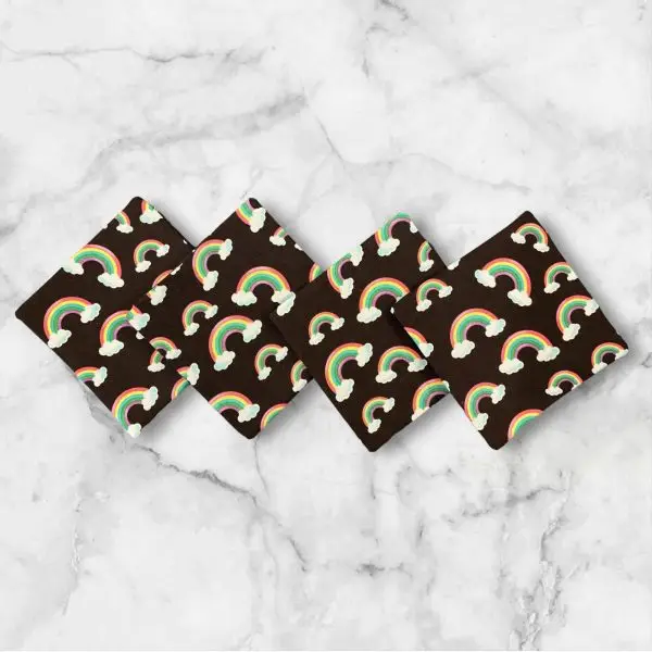 A set of four 4.5-inch square reversible fabric coasters with rainbow designs on one side and polka dots on the other, displayed on a marble background.