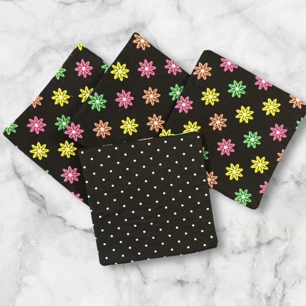 A set of four 4.5-inch square reversible fabric coasters with a colorful starburst pattern on one side and polka dots on the other, displayed on a marble background.