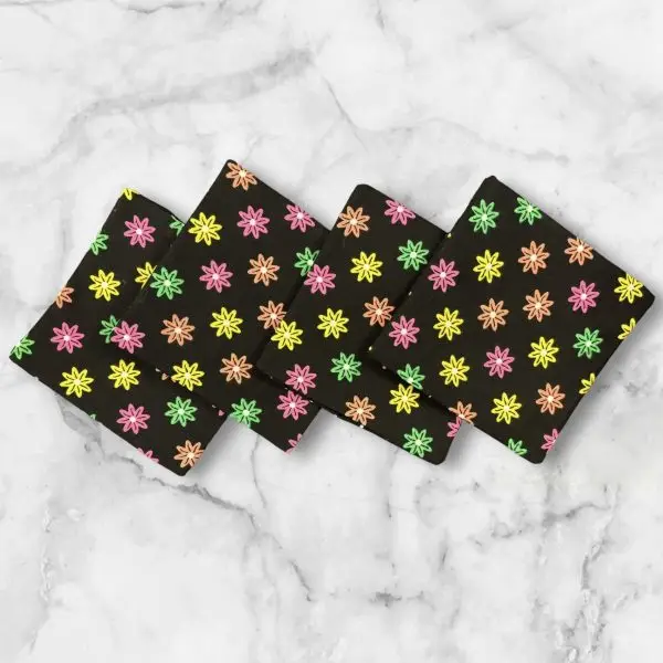 A set of four 4.5-inch square reversible fabric coasters with a colorful starburst pattern on one side and polka dots on the other, displayed on a marble background.