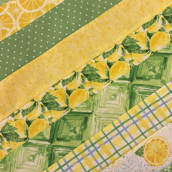 A set of two 19x13 inch fabric placemats, featuring a diagonal patchwork design with green and yellow patterns on one side and a bright lemon slice print on the other, laid on a marble background.