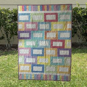 A colorful Jelly Belly Bars Quilt featuring pastel rectangular bars in shades of pink, blue, green, yellow, and purple, measuring 46” x 64”.