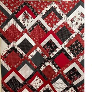 A reversible Ruby Splendor Quilt featuring rich red, black, and white floral patterns on one side and a complementary design on the other, measuring 53” x 70”.