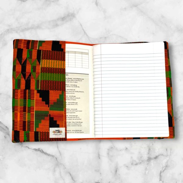 Kente-inspired composition notebook cover featuring bold oranges, greens, blacks, and yellows in intricate geometric patterns with an elastic band.