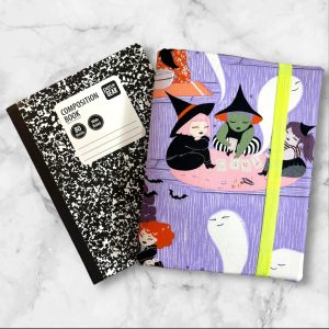 A composition notebook cover featuring a whimsical witch-themed fabric with illustrations of witches, ghosts, and playful scenes in vibrant colors against a lavender background. The cover has a neon green elastic band and is shown next to a standard composition notebook.