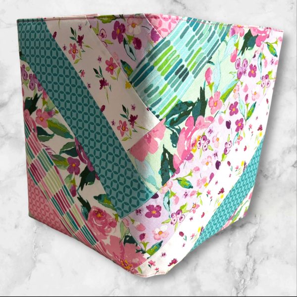 Quilted composition notebook cover with a bright floral design in shades of pink, green, and teal, featuring diagonal stripes and an elastic closure.