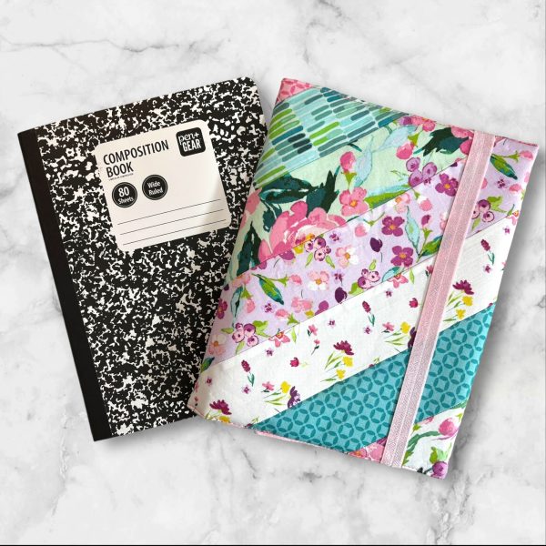 Quilted composition notebook cover with a bright floral design in shades of pink, green, and teal, featuring diagonal stripes and an elastic closure.