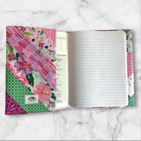 Quilted composition notebook cover with a bright floral design in shades of pink, green, and teal, featuring diagonal stripes and an elastic closure.