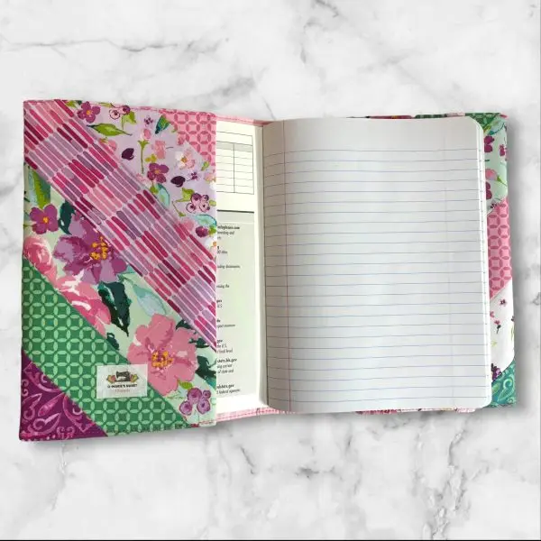 Quilted composition notebook cover with a bright floral design in shades of pink, green, and teal, featuring diagonal stripes and an elastic closure.