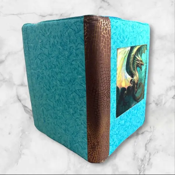 Quilted composition notebook cover with a turquoise and brown design, featuring a detailed illustration of a dragon on the front and an elastic closure.