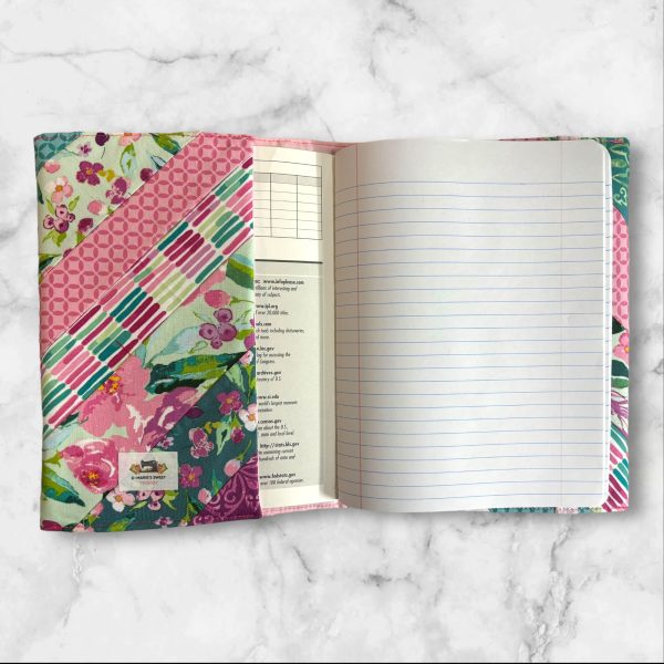 Quilted composition notebook cover with a mix of floral patterns and geometric designs in shades of pink, green, and teal, featuring an elastic closure.