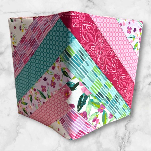 Quilted composition notebook cover with a mix of floral patterns and geometric designs in shades of pink, green, and teal, featuring an elastic closure.