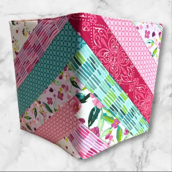 Quilted composition notebook cover with a mix of floral patterns and geometric designs in shades of pink, green, and teal, featuring an elastic closure.