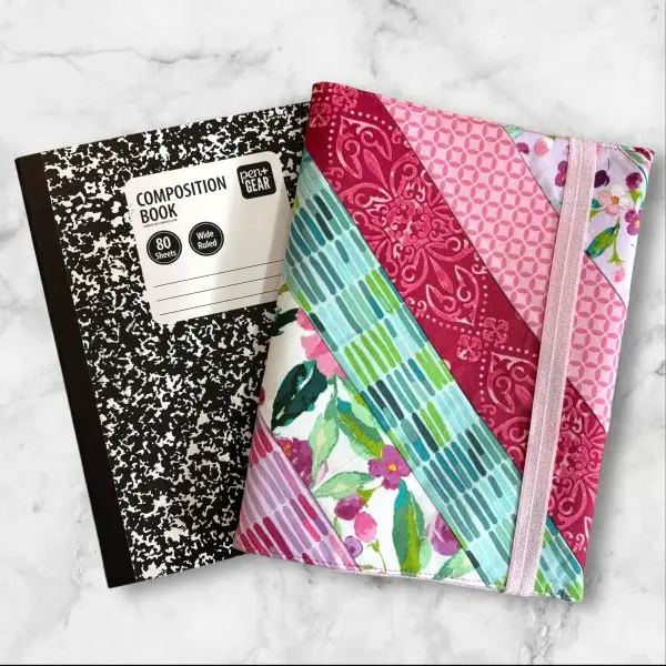 Quilted composition notebook cover with a mix of floral patterns and geometric designs in shades of pink, green, and teal, featuring an elastic closure.