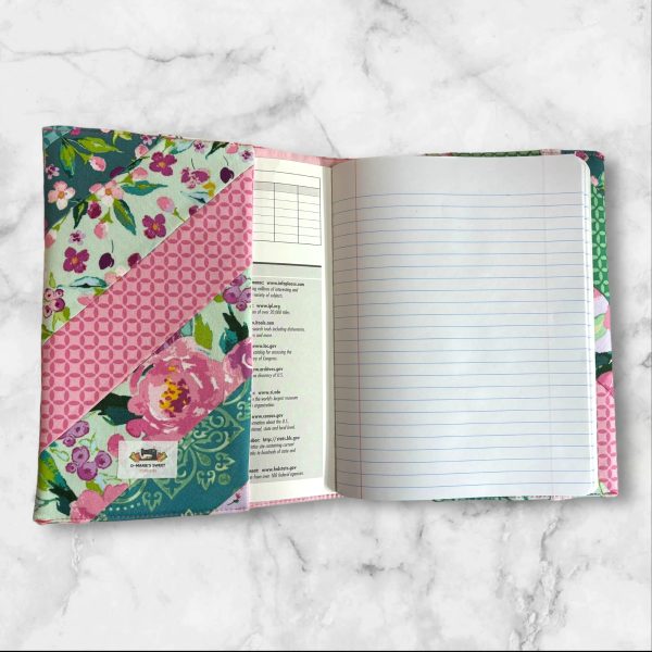 Quilted composition notebook cover with a vibrant floral design in shades of pink, green, and teal, featuring diagonal stripes and an elastic closure.