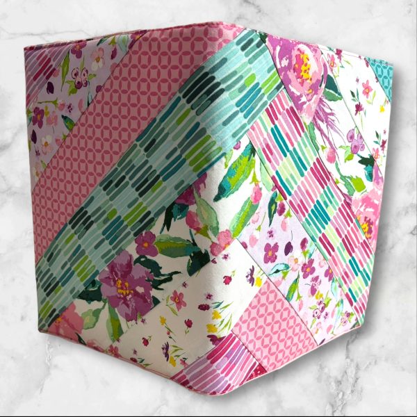 Quilted composition notebook cover with a vibrant floral design in shades of pink, green, and teal, featuring diagonal stripes and an elastic closure.