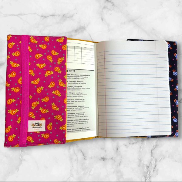 Quilted composition notebook cover with a pink and yellow design, showcasing a playful Cheshire Cat print surrounded by bright floral patterns.