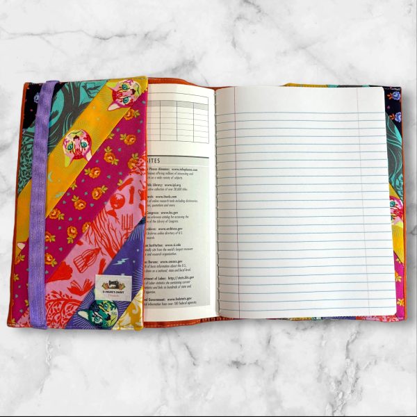 Quilted composition notebook cover with diagonal multicolored stripes, featuring a whimsical illustration of Alice in Wonderland in vibrant, playful colors.