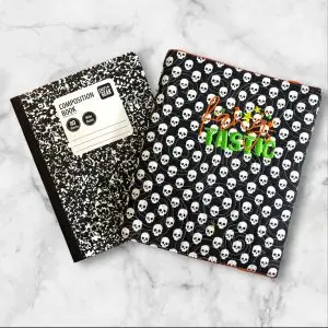 Quilted composition notebook cover in black with white skull print, with "Fang-Tastic" embroidery on the front, is perfect for Halloween or gothic-themed stationery.