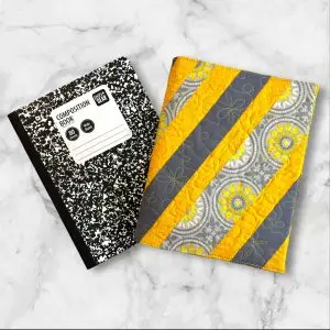 Quilted composition notebook cover with a stylish yellow and gray striped design, adorned with a floral pattern for an elegant look.