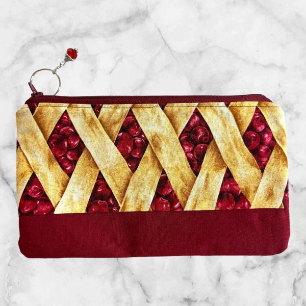 Cherry Pie Zipper Pouch with a design resembling a golden lattice crust and juicy cherries, with a red zipper and bead charm.