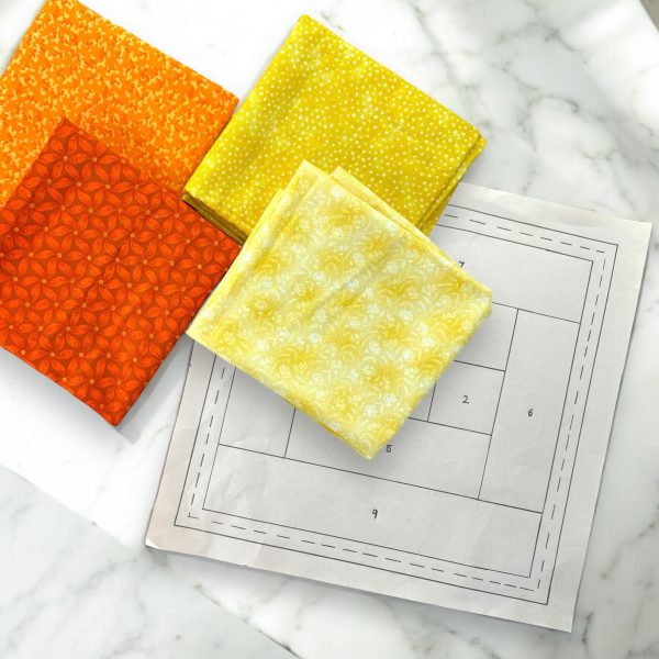 Warm Sunset Tones Log Cabin Paper Piecing Quilt Kit with orange and yellow fabric and quilt block pattern.