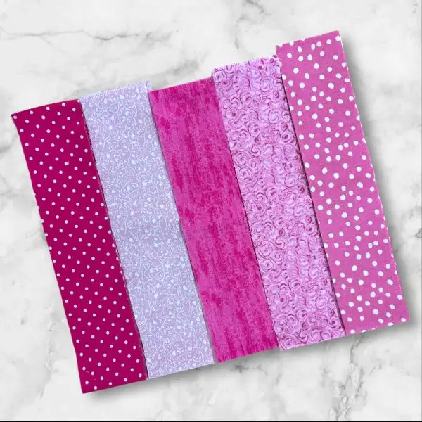 A set of 2.5-inch pink fabric strips featuring 5 different patterns, perfect for quilting and crafting.