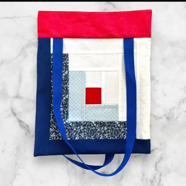 A handmade log cabin-style tote bag in red, blue, and white tones, made from 100% cotton with sturdy nylon straps.