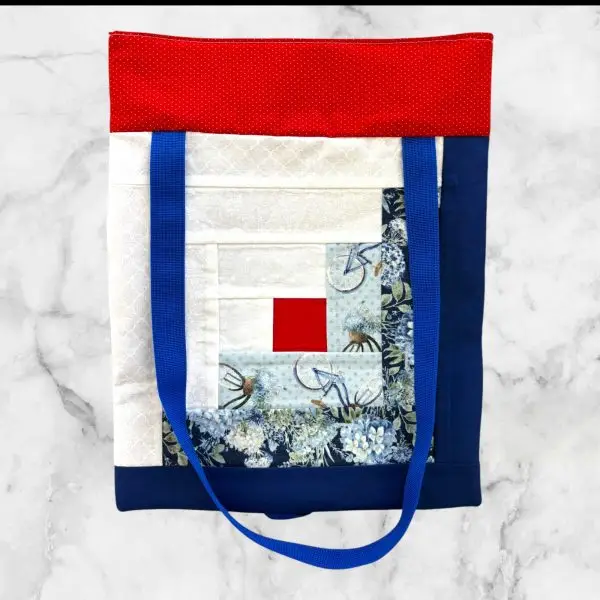 A handmade tote bag featuring a red top with blue-and-white striped fabric and sturdy blue nylon straps, crafted from 100% cotton.