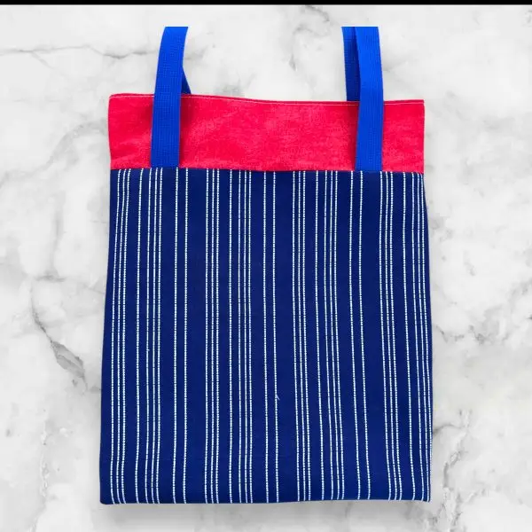 A handmade log cabin-style tote bag in red, blue, and white tones, made from 100% cotton with sturdy nylon straps.