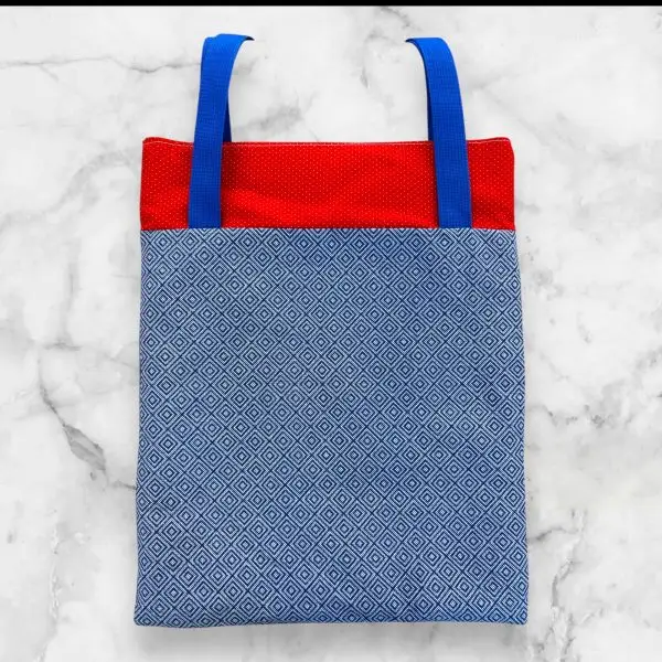 A handmade tote bag featuring a red top with blue-and-white striped fabric and sturdy blue nylon straps, crafted from 100% cotton.