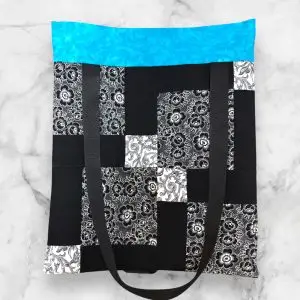 A handmade quilt block tote bag featuring a patchwork front with black-and-white patterns, a turquoise accent, and a vine-print back.