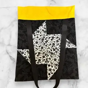 A handmade quilt block tote bag featuring a black-and-white pinwheel front with a yellow accent and a swirl-print back.