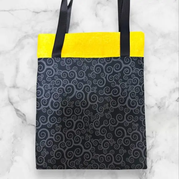 A handmade quilt block tote bag featuring a black-and-white pinwheel front with a yellow accent and a swirl-print back.