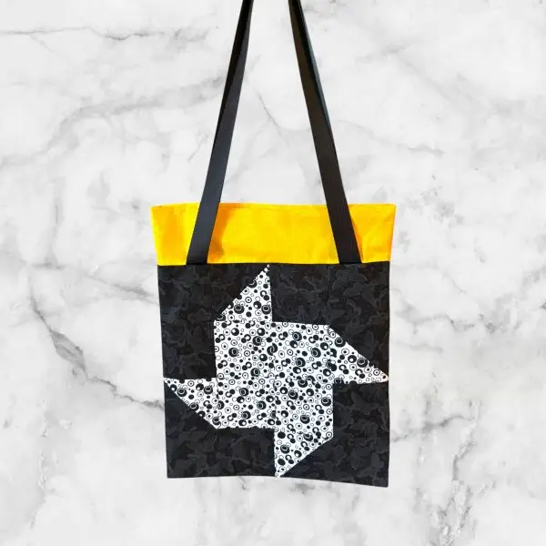 A handmade quilt block tote bag featuring a black-and-white pinwheel front with a yellow accent and a swirl-print back.