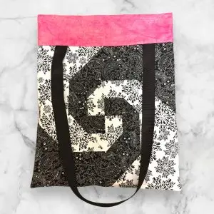 A handmade quilt block tote bag featuring a black-and-white spiral front with a pink accent and a polka dot-patterned back.